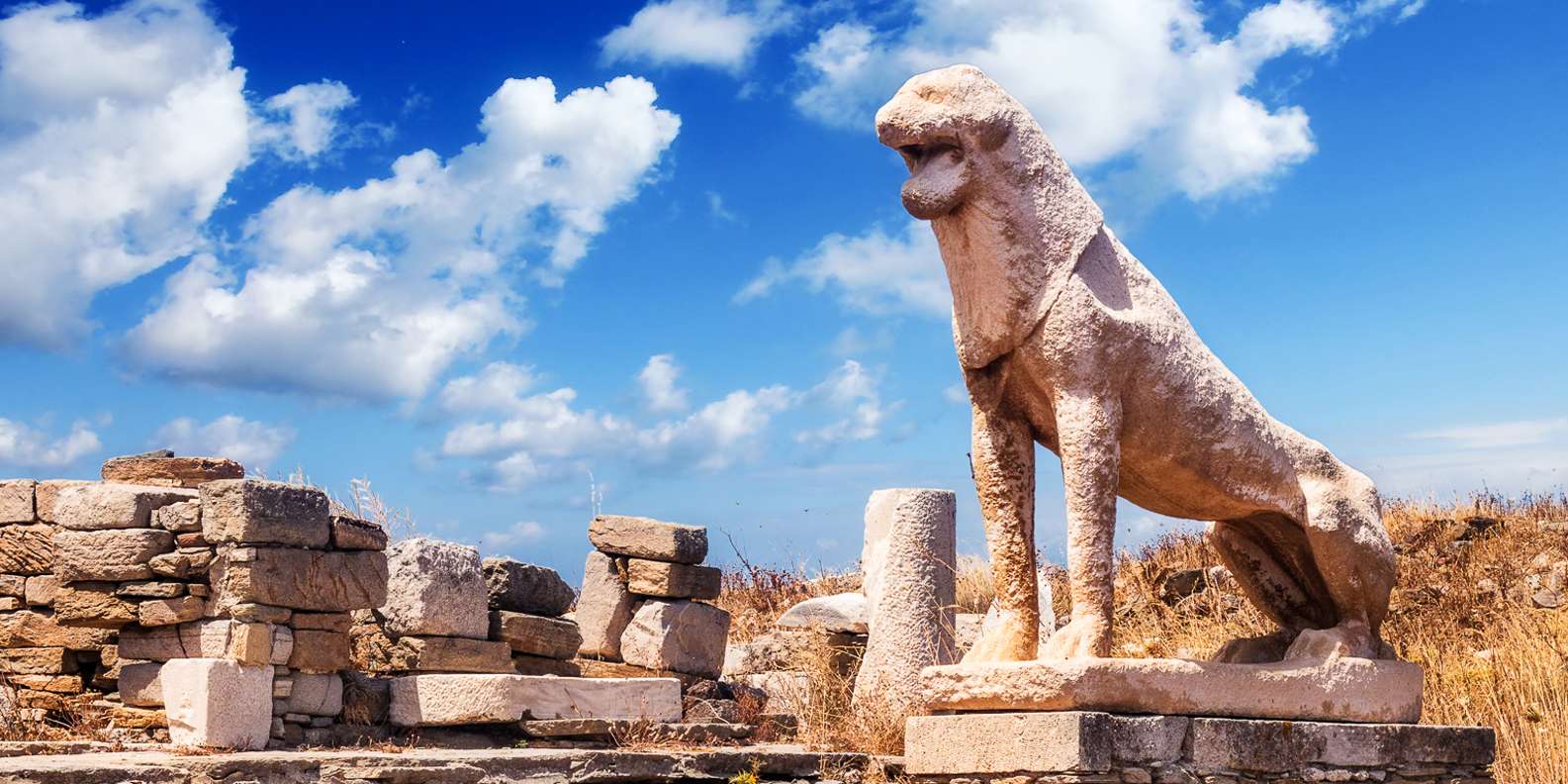 Ancient marble columns and lion statues on Delos island with turquoise Aegean waters and Mykonos visible across the channel, archaeological island photography