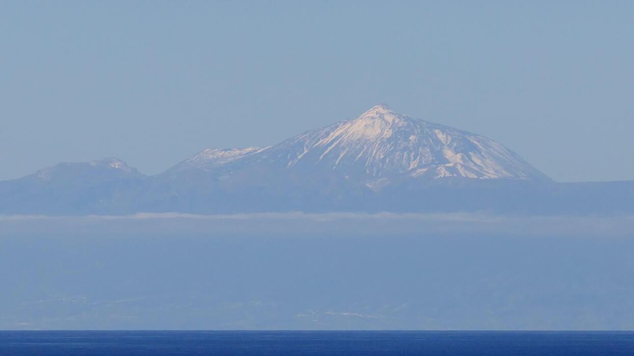 Mount Teide volcanic peak rising above clouds on Tenerife island with dry volcanic terrain and blue Atlantic Ocean below, dramatic landscape photography