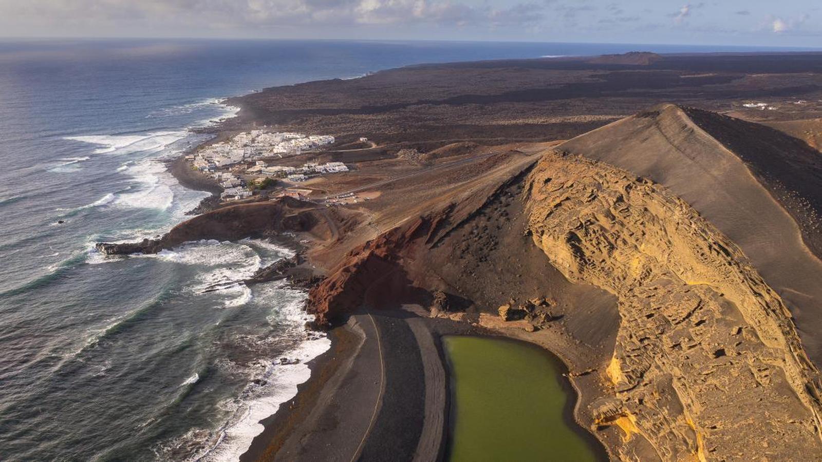 Dramatic volcanic landscape of Timanfaya National Park in Lanzarote with red and black lava fields stretching toward Atlantic coast under clear blue sky, nature photography