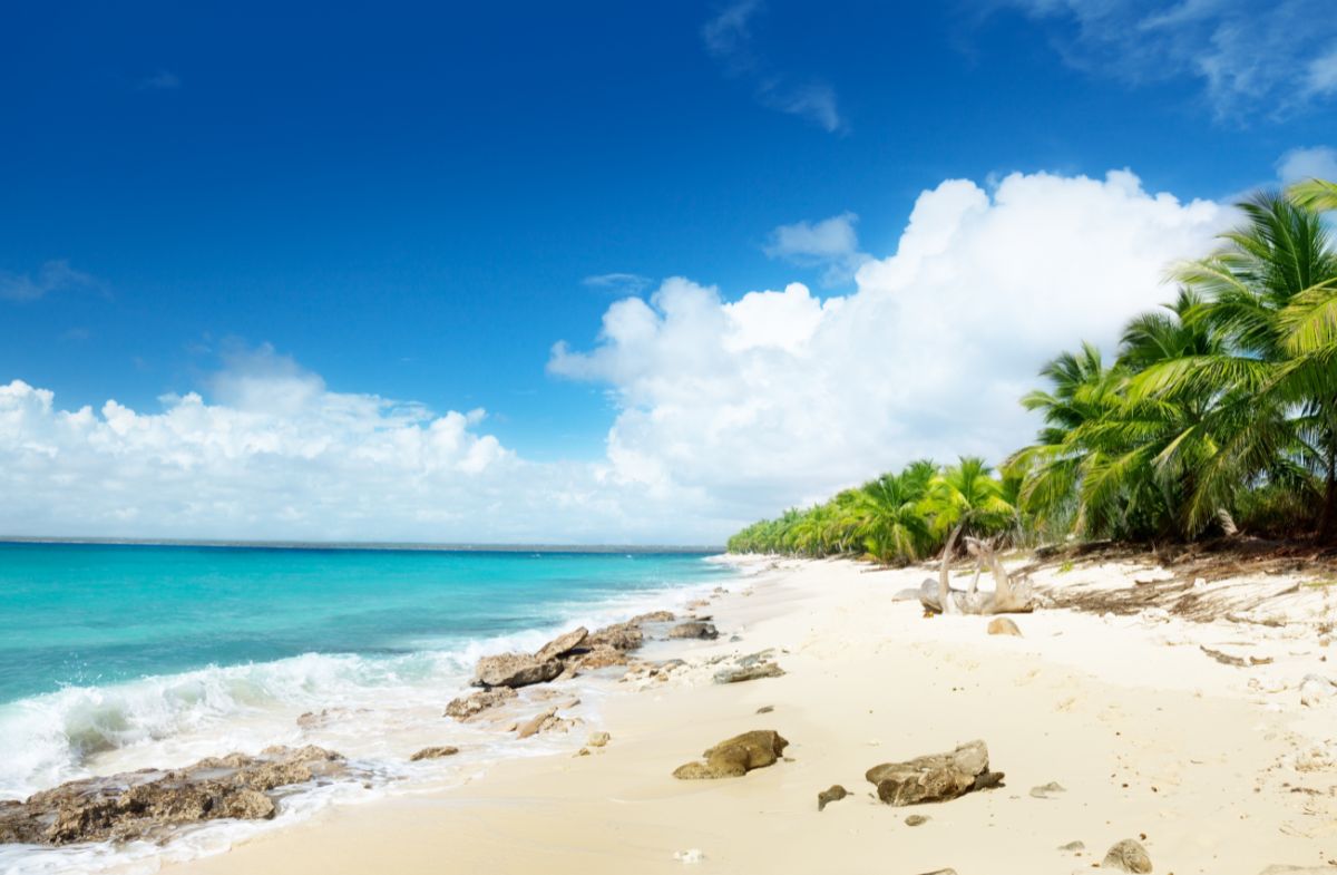 Tropical white sand beach of Isla Catalina with crystal clear shallow waters and lush green hills of Dominican Republic coast in background, private island photography