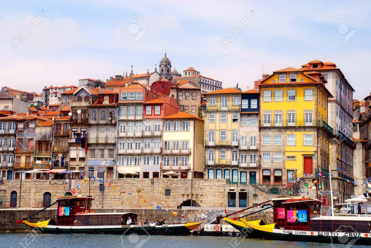 Porto Ribeira district with colorful buildings descending to the Douro riverfront and traditional rabelo boats with port wine barrels in warm afternoon light, Portuguese heritage photography