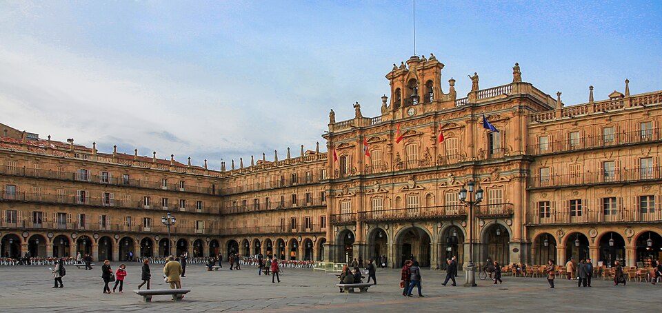 Salamanca Plaza Mayor with ornate baroque sandstone facades and arched colonnades in warm evening light with university students crossing the square, Spanish heritage photography
