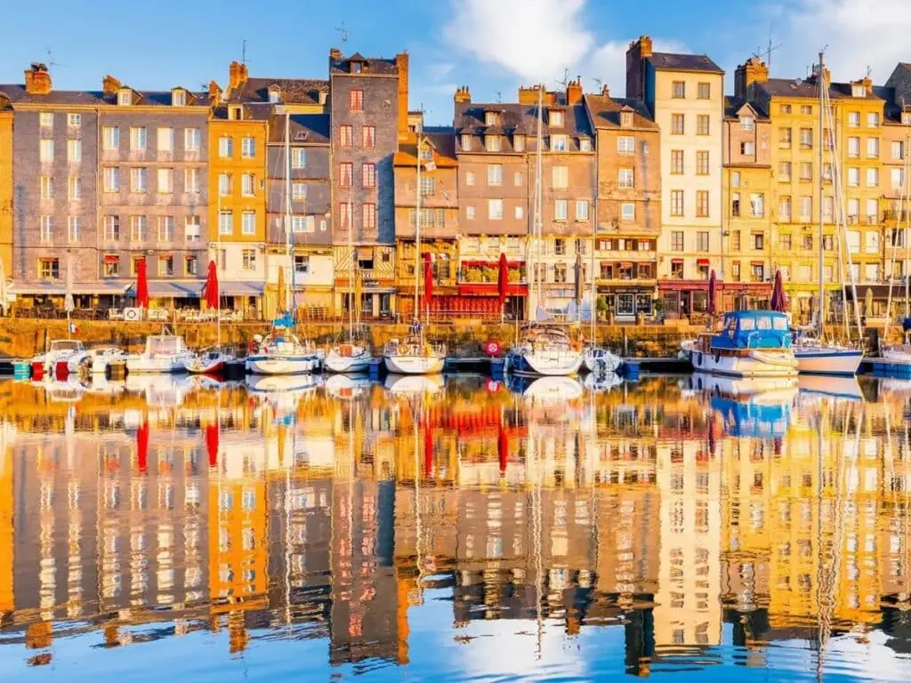 Honfleur old harbor with tall colorful slate-fronted houses reflected in calm water and sailboats moored along the quay in warm evening light, Norman coastal photography