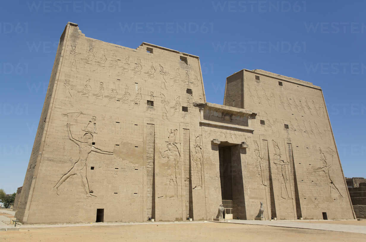 Temple of Horus at Edfu with massive stone pylon entrance and hieroglyphic walls seen from approach corridor in bright morning desert light, ancient Egyptian photography