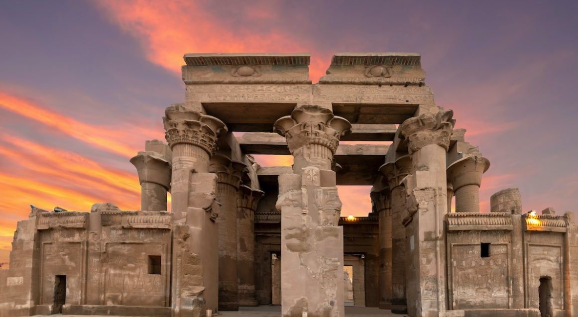 Kom Ombo temple perched on elevated bank above the Nile river at sunset with double columns and crocodile reliefs visible in warm golden light, riverside archaeology photography