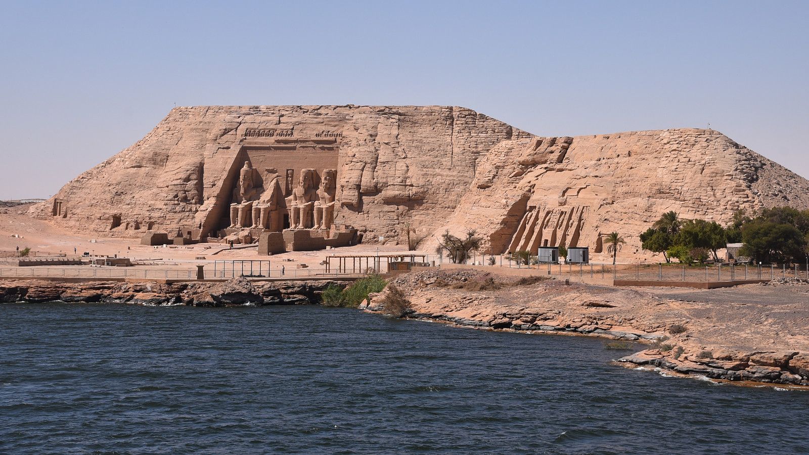 Four colossal statues of Ramesses II at Abu Simbel temple facade carved into sandstone cliff face in bright desert morning light with Lake Nasser visible, monumental Egyptian photography