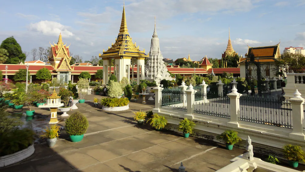 Royal Palace of Phnom Penh with golden spires and Silver Pagoda reflected in manicured gardens with Mekong river visible in background, Cambodian heritage photography