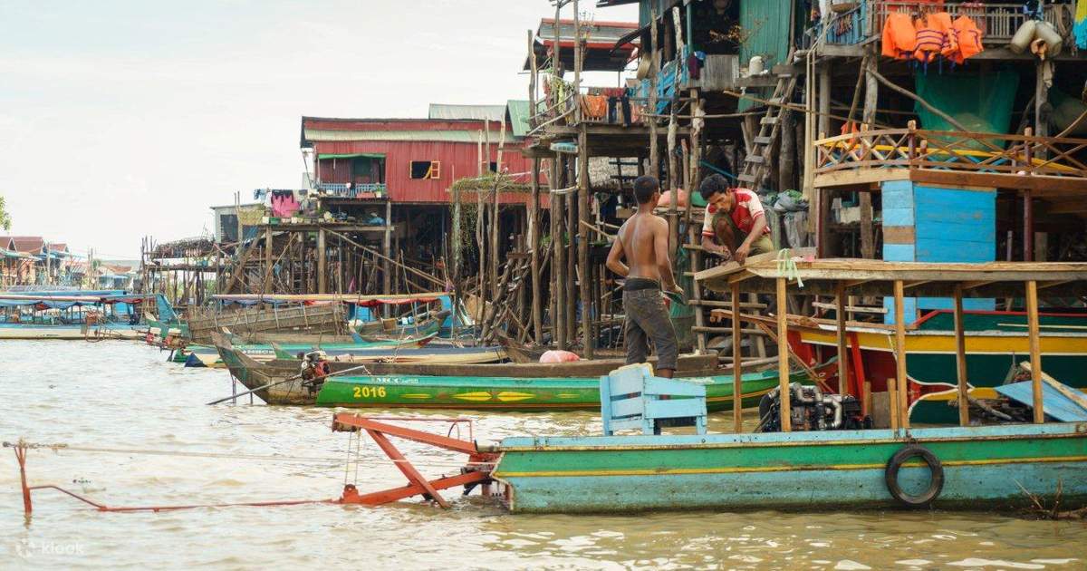 Floating village on Tonlé Sap lake with wooden houses on stilts and fishing boats on calm reflective water in soft morning mist, Cambodian lake life photography