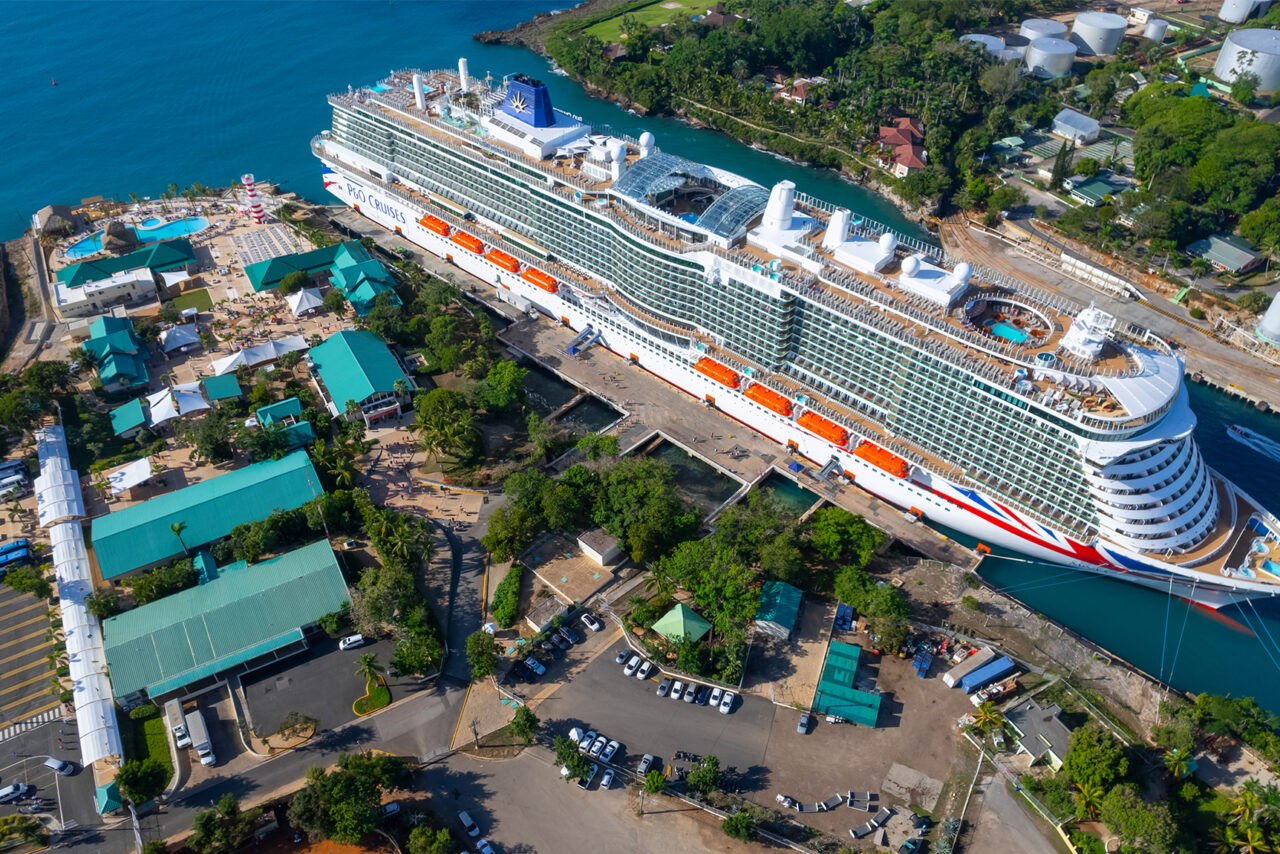 Cruise ship docked at La Romana port in Dominican Republic with palm-lined waterfront and calm Caribbean waters in warm morning light, tropical embarkation photography