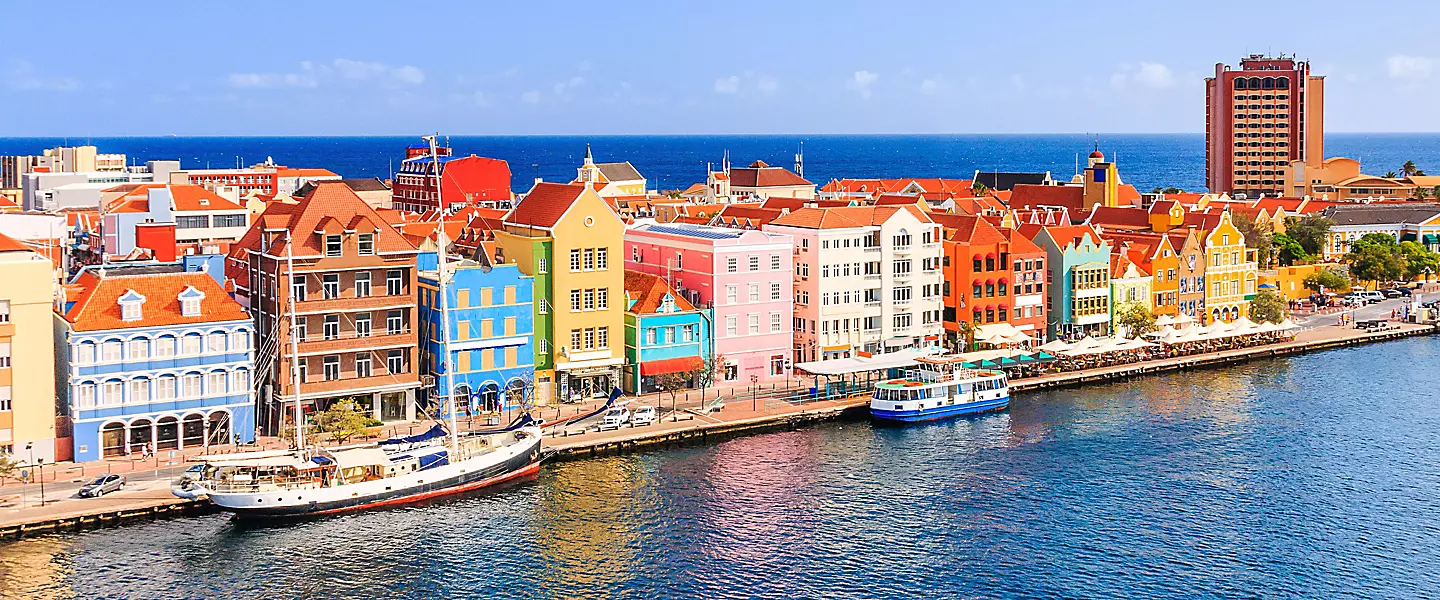 Pastel-colored Dutch colonial facades lining the waterfront of Willemstad Curaçao with Queen Emma pontoon bridge and turquoise harbor waters, UNESCO heritage photography