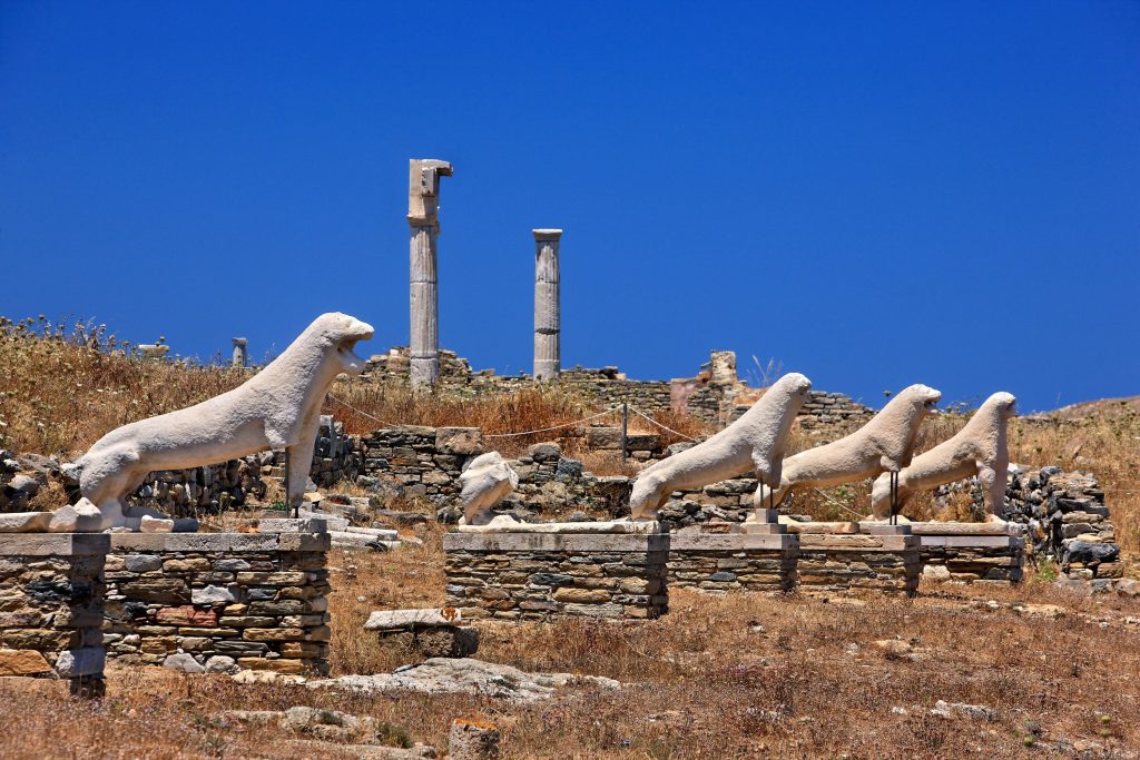 Terrace of the Lions ancient marble statues on Delos island Greece with dry archaeological landscape and Aegean Sea in background, UNESCO heritage site photography