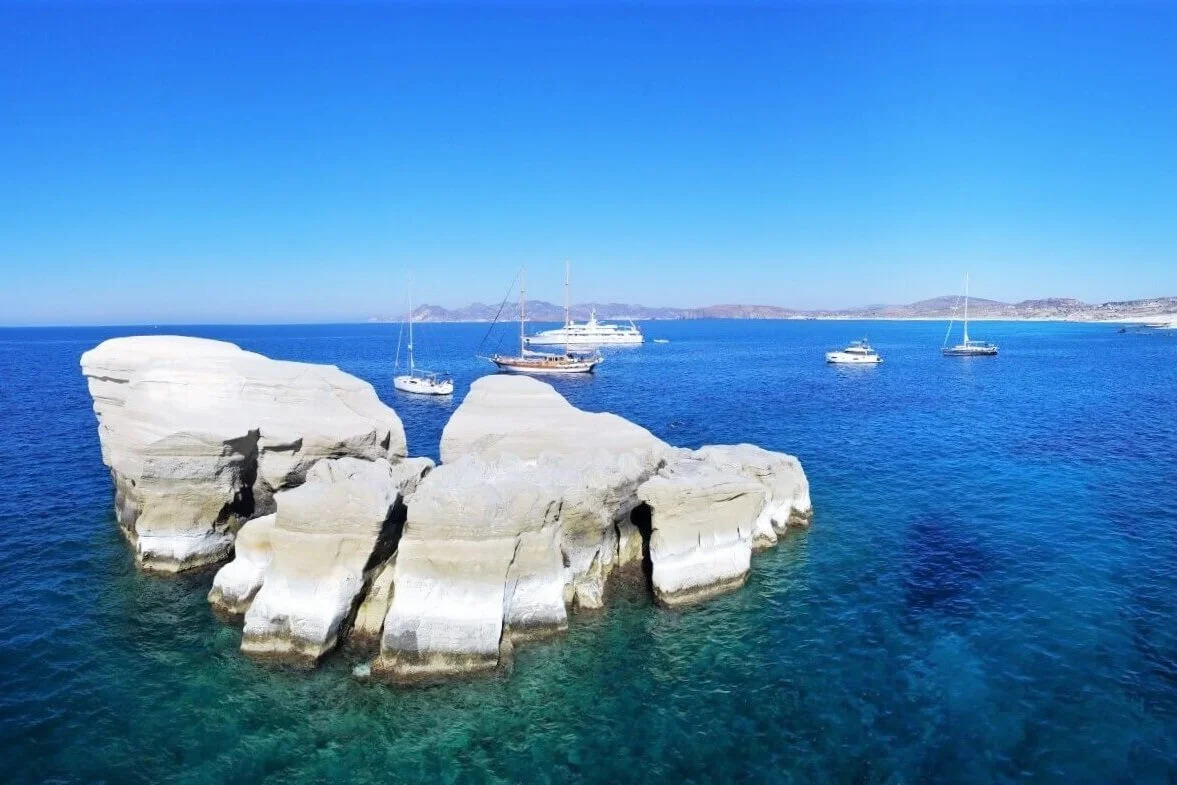 Sarakiniko lunar white rock formations meeting turquoise water on Milos island Greece with small boat anchored in sheltered cove, volcanic geology travel photography