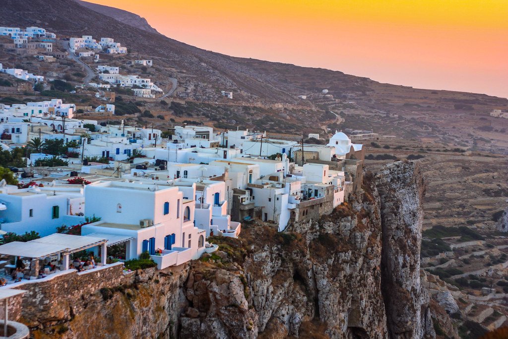 Folegandros clifftop Chora village at dusk perched on edge of steep Aegean cliff with bougainvillea and warm taverna lights, intimate Greek island atmosphere photography