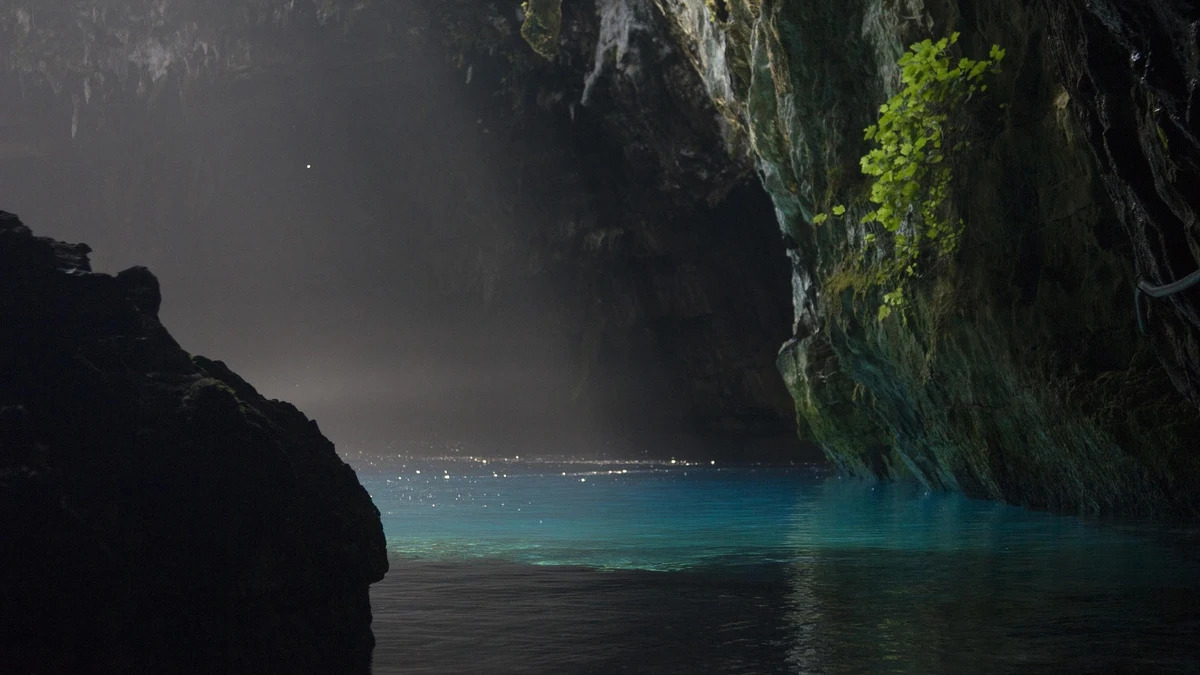 Melissani Cave on Kefalonia island with turquoise water illuminated by natural sunlight through collapsed ceiling and lush vegetation framing the opening, Greek nature photography