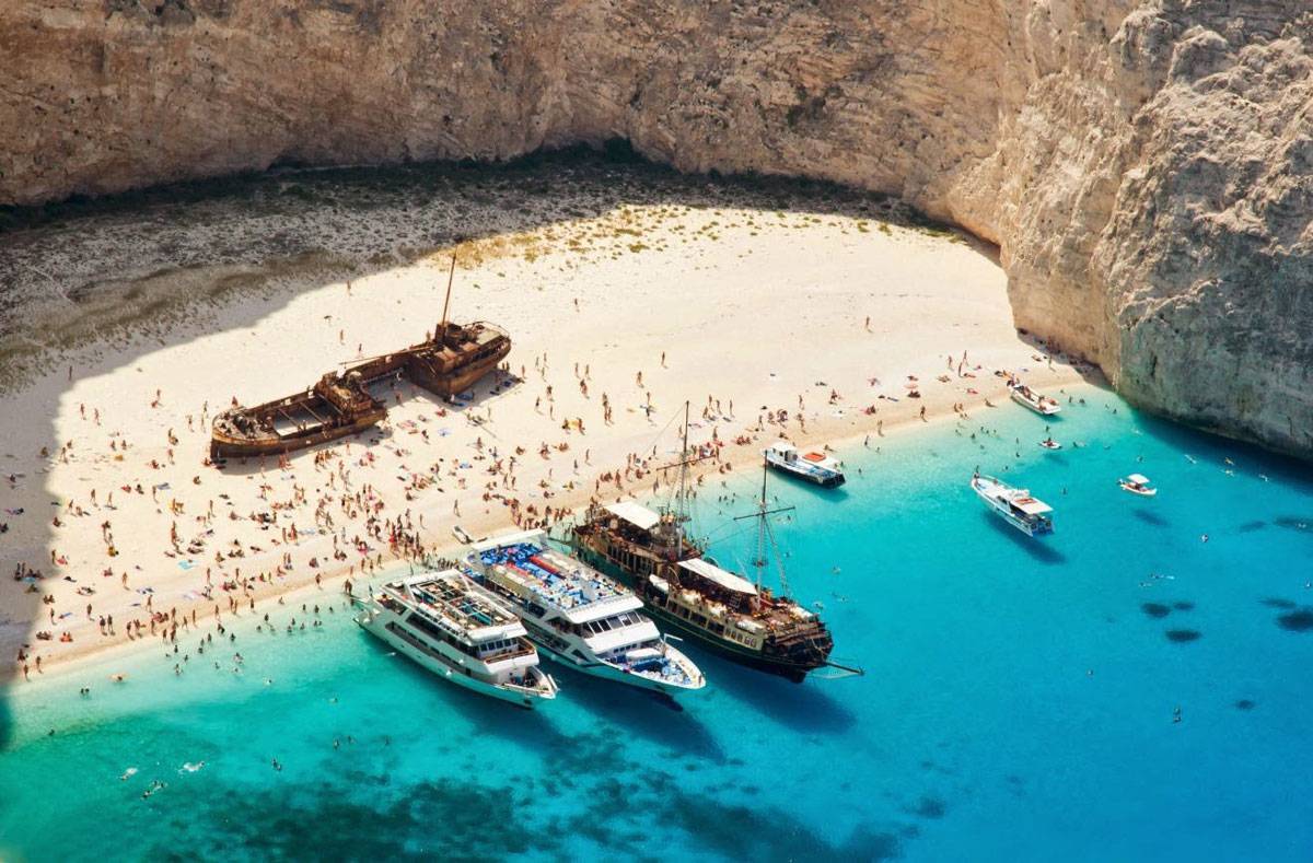 Navagio Beach Zakynthos from above with turquoise water inside white limestone cove and rusty shipwreck on sand, dramatic Ionian Sea cliff scenery, aerial travel photography