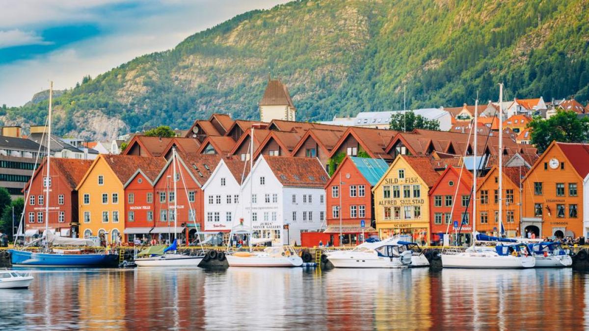 Bergen Bryggen wharf colorful wooden Hanseatic buildings along harbor waterfront with mountains rising behind in soft morning light, Norwegian heritage travel photography