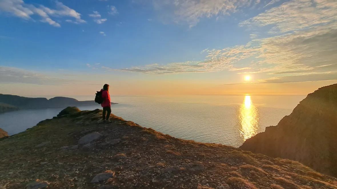 North Cape cliff plateau at midnight sun with dramatic 307-meter drop to the Barents Sea and vast open Arctic horizon, warm orange light on stark tundra landscape, expedition photography