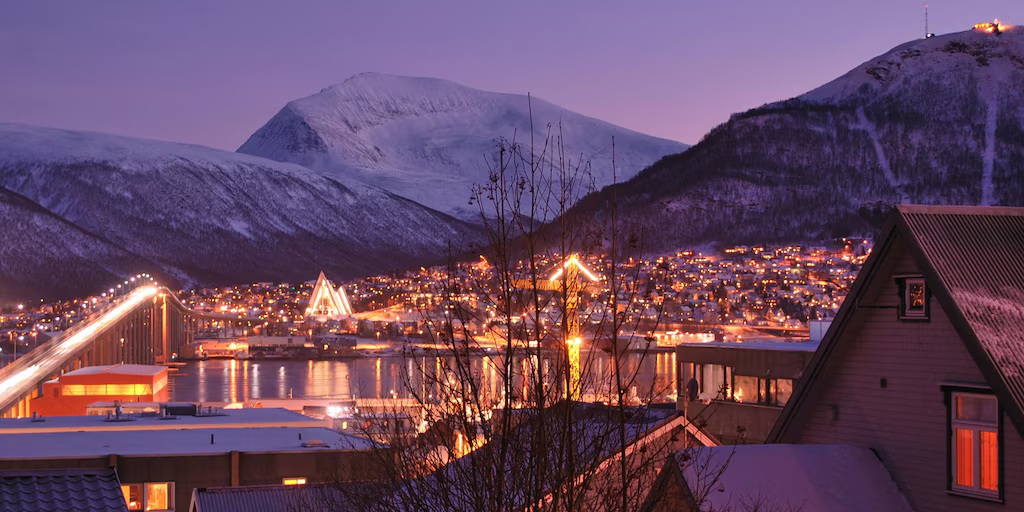 Tromsø Arctic cityscape during polar night blue twilight with Arctic Cathedral illuminated and snow-covered mountains behind, deep blue winter sky, Norwegian winter travel photography