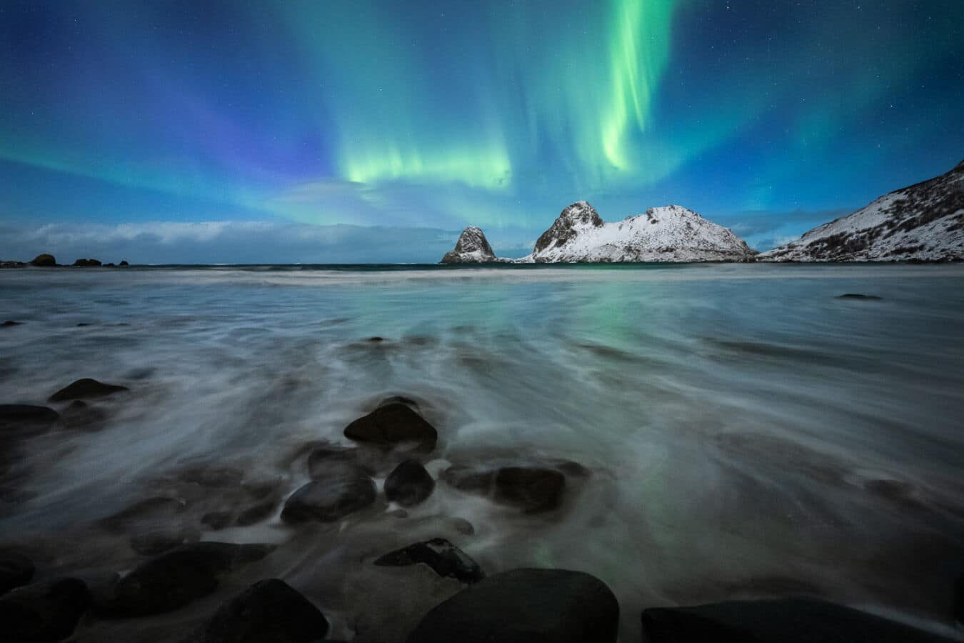 Vesterålen islands Norway winter coastline with steep dark mountains framing calm fjord water and faint aurora glow reflecting on surface, isolated fishing village lights in distance, Arctic night photography
