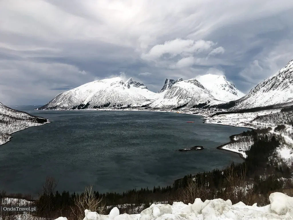 Senja island Norway jagged winter peaks rising from Norwegian Sea with snow-covered ridges and dark Arctic water below, moody blue hour light, dramatic Scandinavian landscape photography