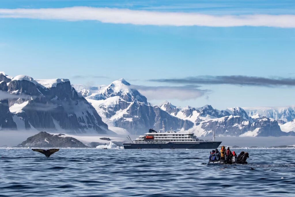 Antarctic Peninsula icebergs and glaciers with expedition ship navigating between massive blue ice formations under overcast