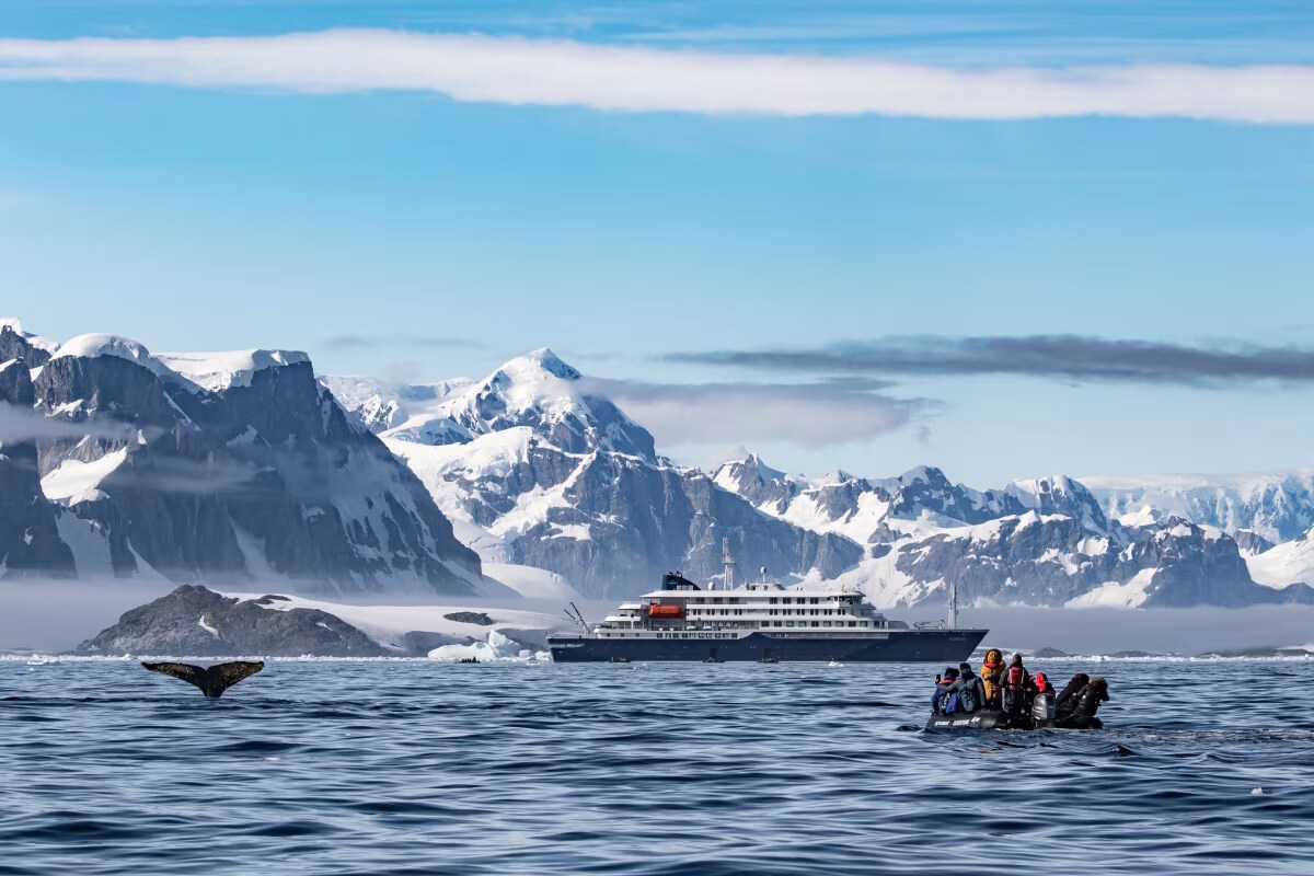 Antarctic Peninsula icebergs and glaciers with expedition ship navigating between massive blue ice formations under overcast polar sky, pristine white landscape, polar expedition photography