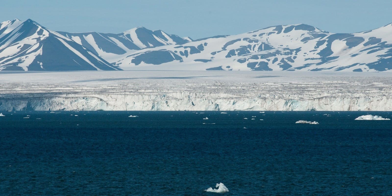 Hornsund fjord Svalbard with massive tidewater glacier calving into dark Arctic water and jagged mountain peaks under cloudy polar sky, expedition zodiac approaching ice face, Arctic photography