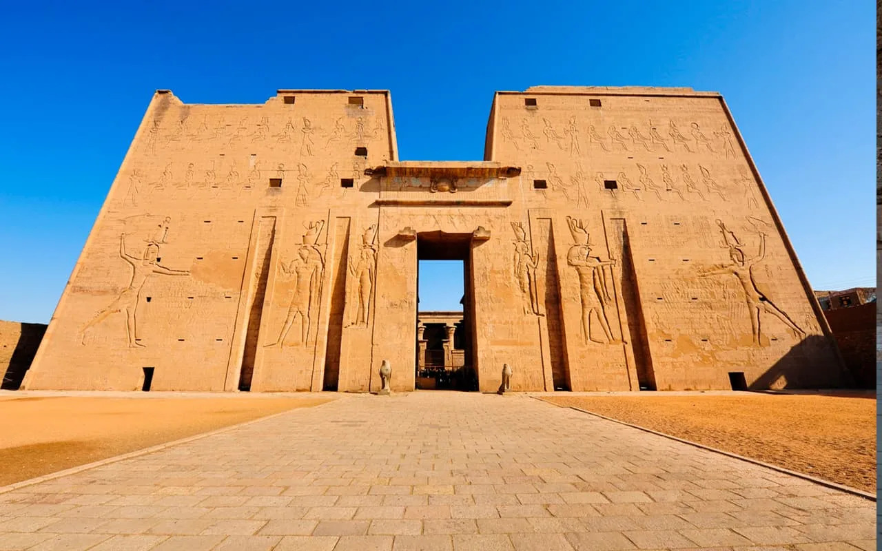 Temple of Horus at Edfu massive stone entrance pylon with carved falcon god reliefs and hieroglyphics in warm afternoon light, best preserved Ptolemaic temple, Egyptian archaeology photography