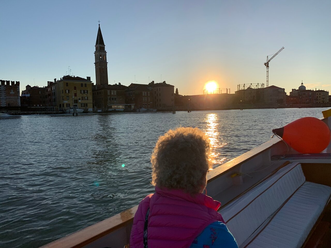 Venice waterfront at dawn with historic buildings and gondolas along Grand Canal as small cruise ship departs toward the open Adriatic Sea, warm Italian morning light, travel photography