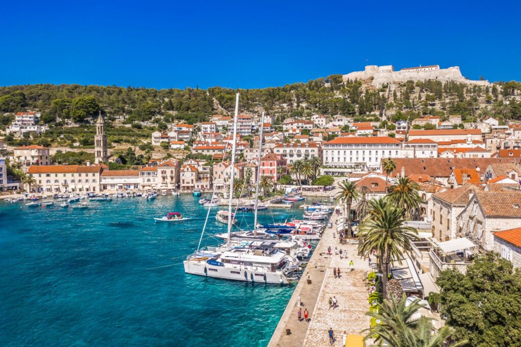 Hvar island harbor with Venetian stone fortress above turquoise Adriatic water and traditional stone buildings along the waterfront, warm Mediterranean evening light, Croatian island photography