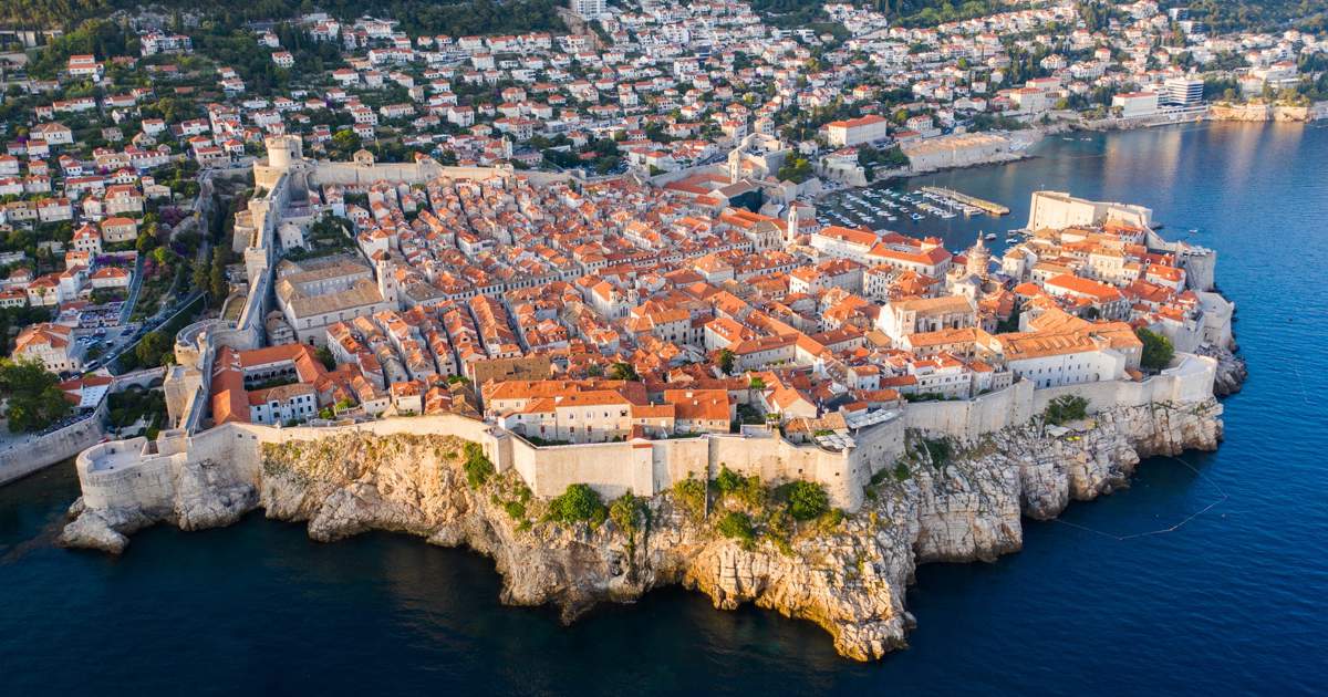 Dubrovnik old town from above with medieval stone walls encircling terracotta rooftops and turquoise Adriatic Sea beyond, dramatic Croatian coastal heritage, UNESCO site travel photography