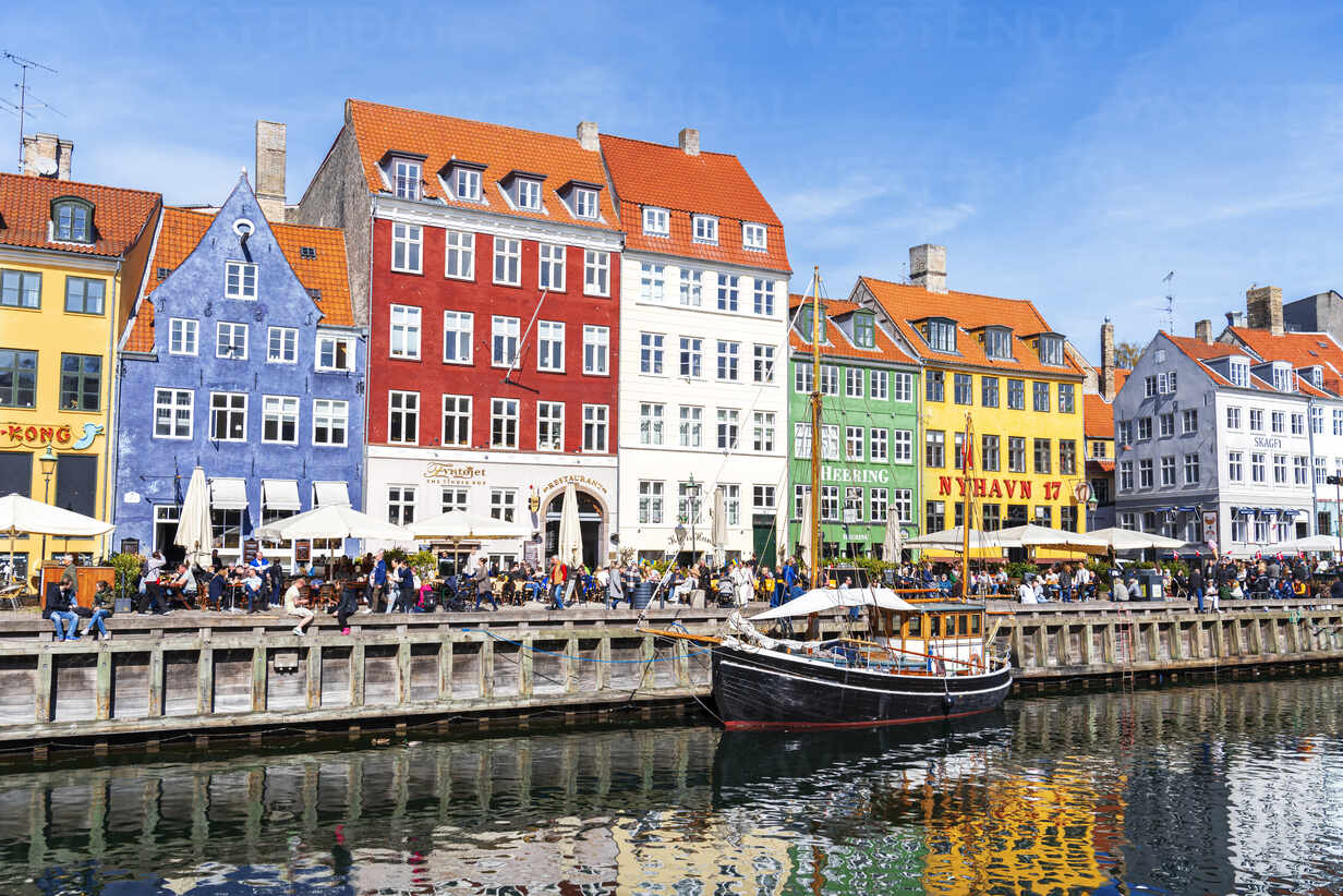 Nyhavn Copenhagen colorful canal-side townhouses with traditional sailing boats moored along the waterfront and cafe terraces in warm Scandinavian summer light, Danish capital travel photography