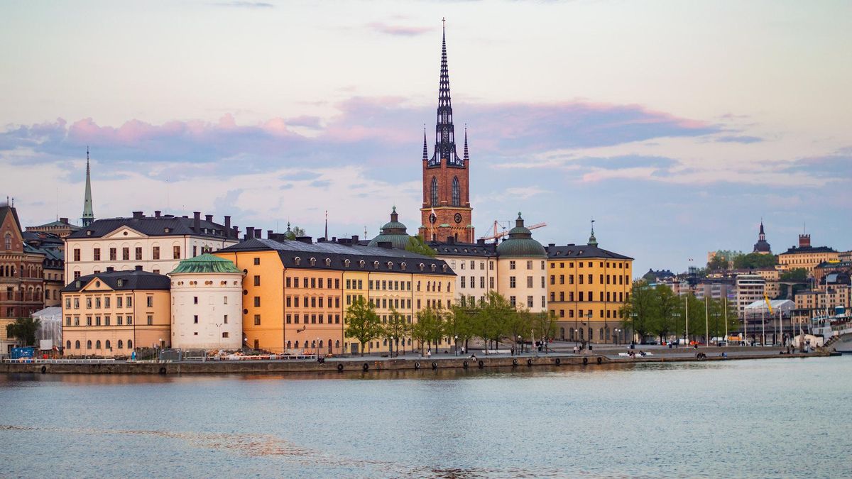 Gamla Stan Stockholm old town island with medieval buildings and church spires seen from the water with passenger ship approaching through Swedish archipelago, warm golden hour light, Nordic travel photography