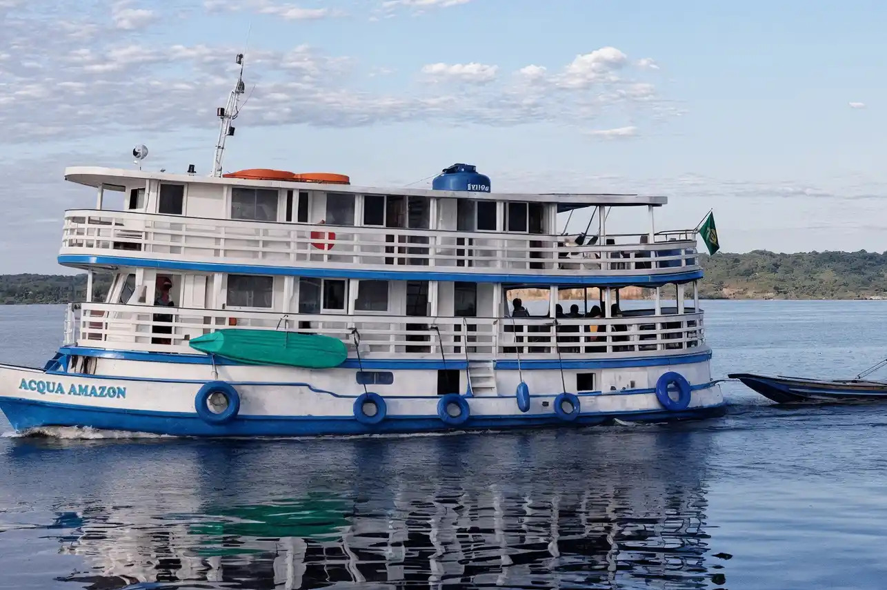 Small expedition cruise ship anchored on the Rio Negro in the Brazilian Amazon at golden hour with dense rainforest canopy reflecting in dark still water, tropical wilderness travel photography