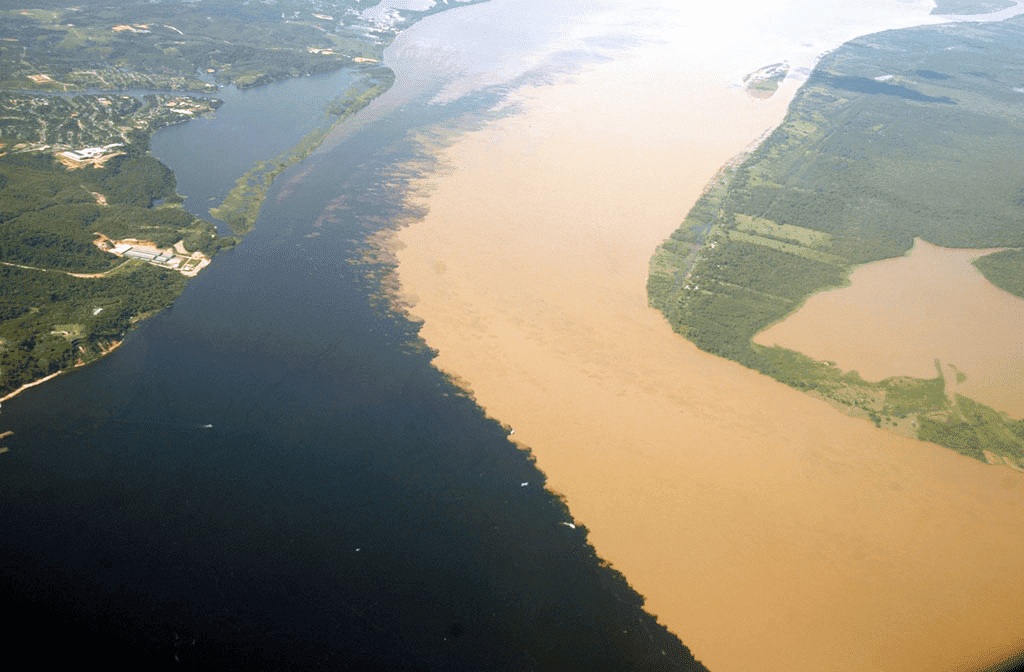 Meeting of the Waters near Manaus where dark Rio Negro and sandy Solimões rivers flow side by side without mixing, aerial view showing sharp color boundary, Brazilian Amazon natural phenomenon photography