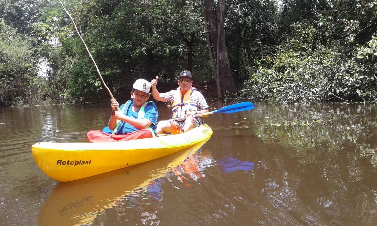 Kayak expedition through Anavilhanas archipelago flooded forest with dense canopy reflecting in dark still water and lush vegetation framing narrow waterway, Brazilian Amazon expedition photography