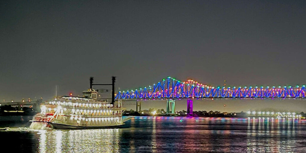 Paddlewheeler cruise ship navigating the Mississippi River at golden hour with lush green riverbanks and Spanish moss hanging
