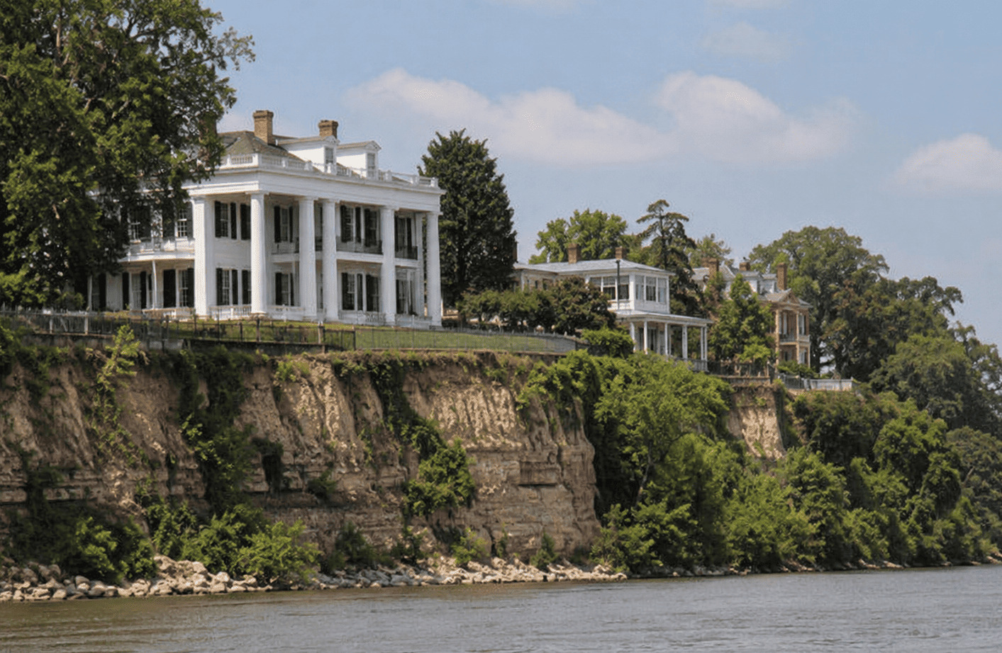Natchez Mississippi historic antebellum mansions perched on green river bluffs above the Mississippi River with paddlewheeler docked at the waterfront below, warm afternoon light, Southern heritage photography