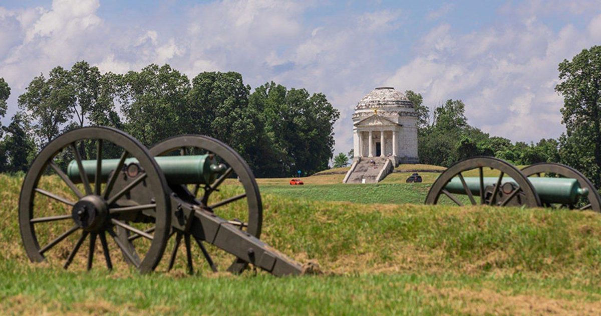 Vicksburg National Military Park with Civil War monuments and cannon on green rolling hillside overlooking the Mississippi River, warm golden hour light, American historical battlefield photography