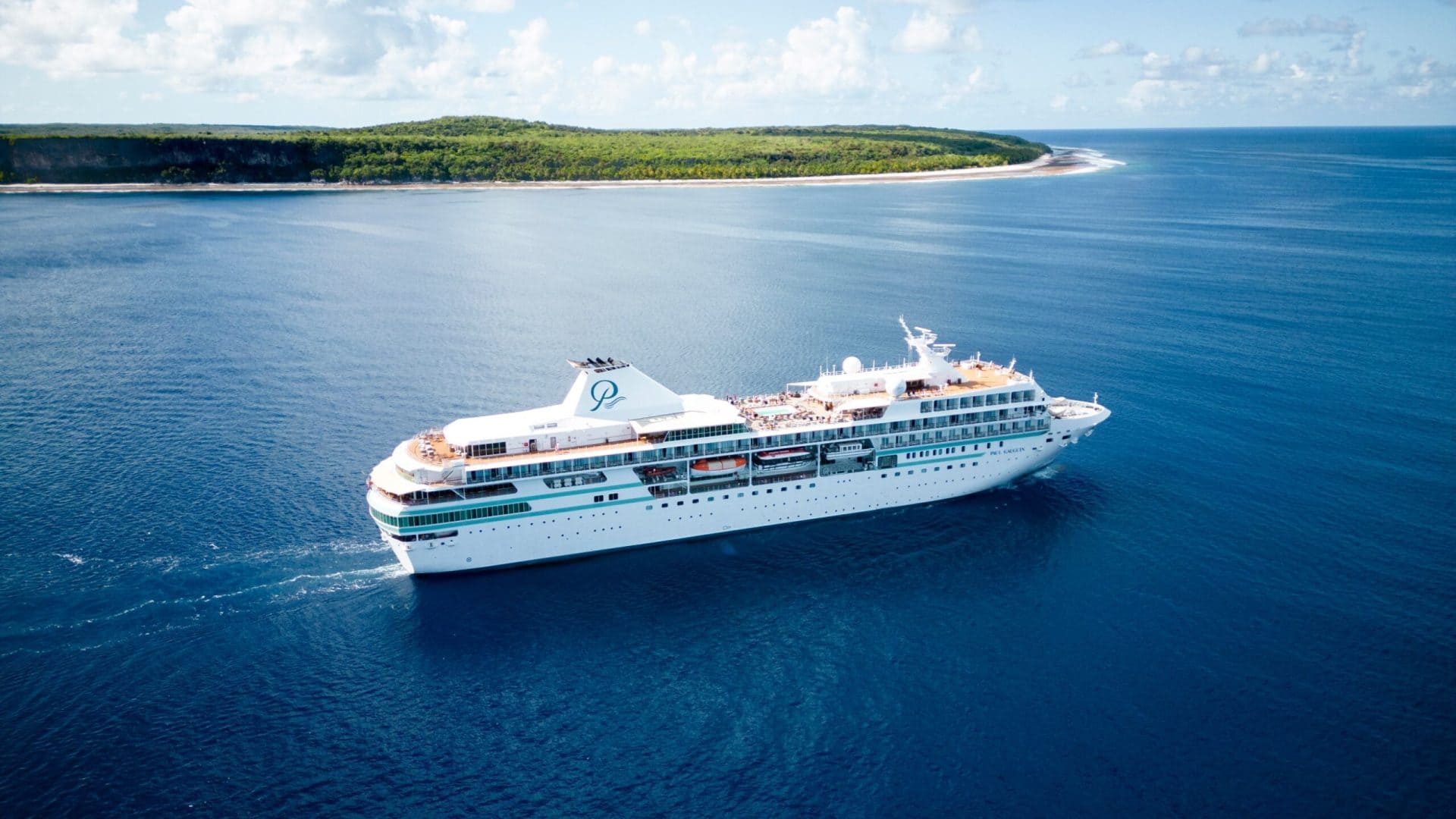 Small cruise ship anchored inside turquoise Bora Bora lagoon with Mount Otemanu volcanic peak rising behind and overwater reef visible beneath clear water, French Polynesia travel photography