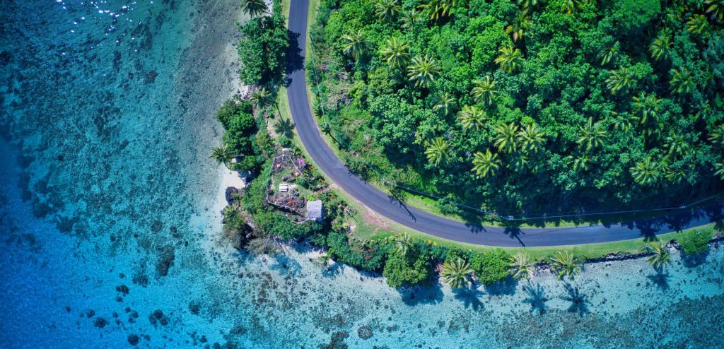 Huahine island lush tropical vegetation covering volcanic hills with shallow turquoise lagoon in foreground and traditional outrigger canoe on calm water, untouched Polynesian island photography