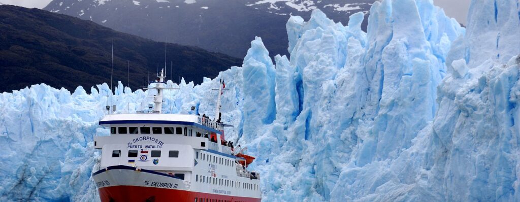 Expedition ship navigating narrow Chilean fjord channel with towering granite walls and hanging glaciers on both sides under