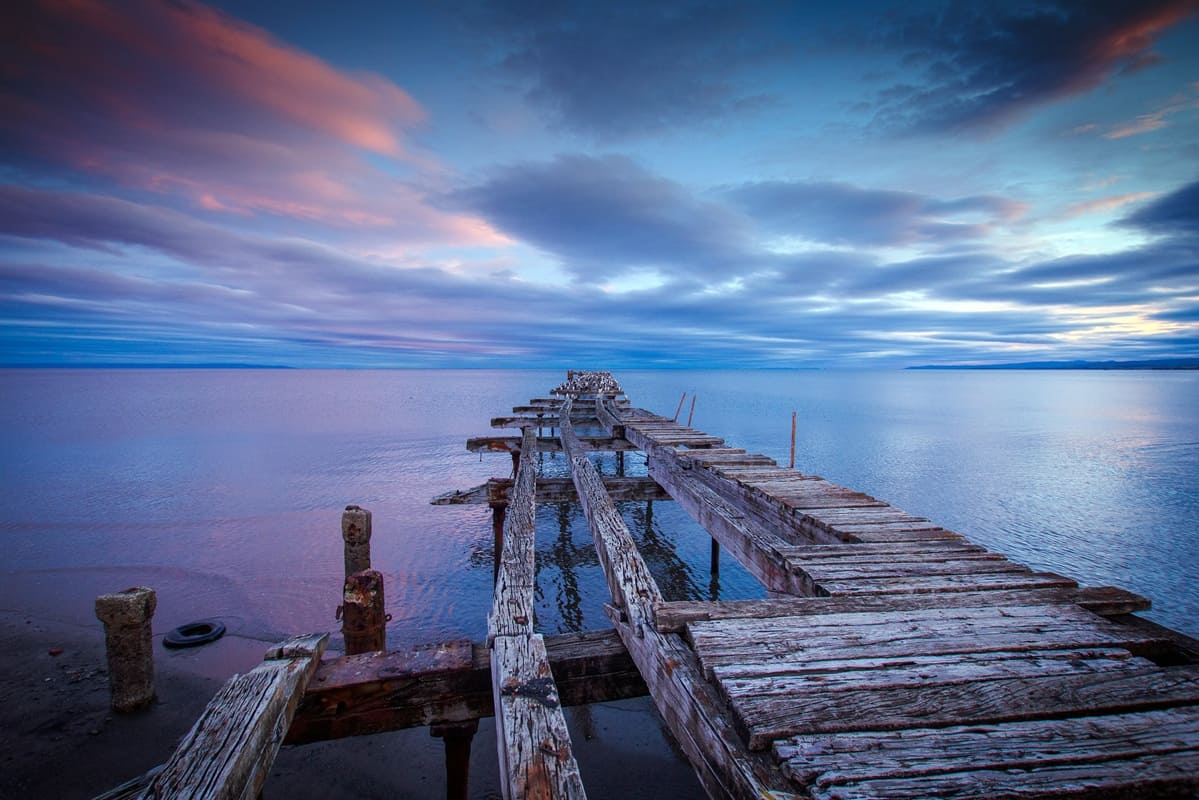 Punta Arenas waterfront with Strait of Magellan stretching to distant Tierra del Fuego under wide Patagonian sky, expedition ship docked at port, windswept southern Chile travel photography