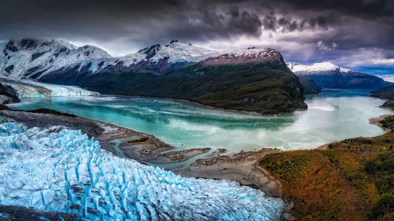 Narrow Chilean fjord channel with steep granite walls draped in temperate rainforest and waterfalls cascading into dark glacial water, expedition ship visible in distance, Patagonian wilderness photography