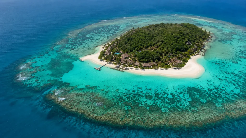 Aerial view of Fiji private island with white sand beach turquoise lagoon and lush tropical vegetation surrounded by coral re