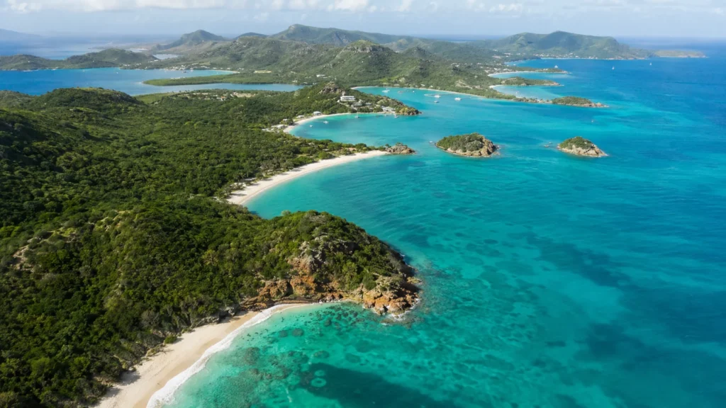 Aerial view of Antigua coastline with turquoise Caribbean water multiple white sand coves and green hillsides, bright tropica