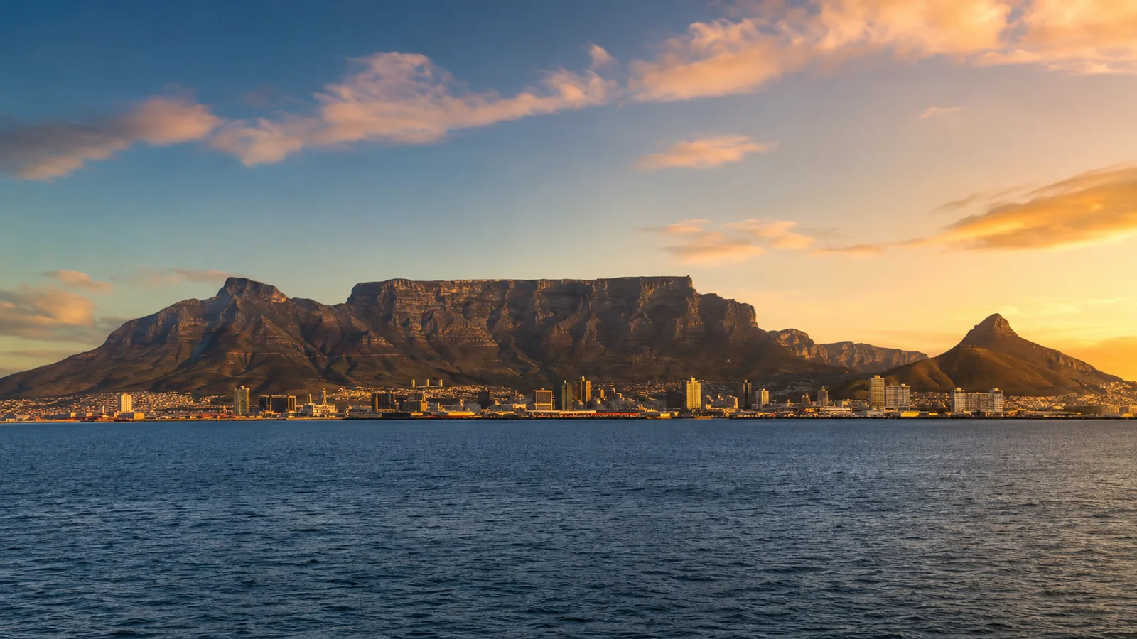 Cape Town skyline with Table Mountain behind the city and ocean in the foreground at sunset, warm golden light, luxury city travel photography