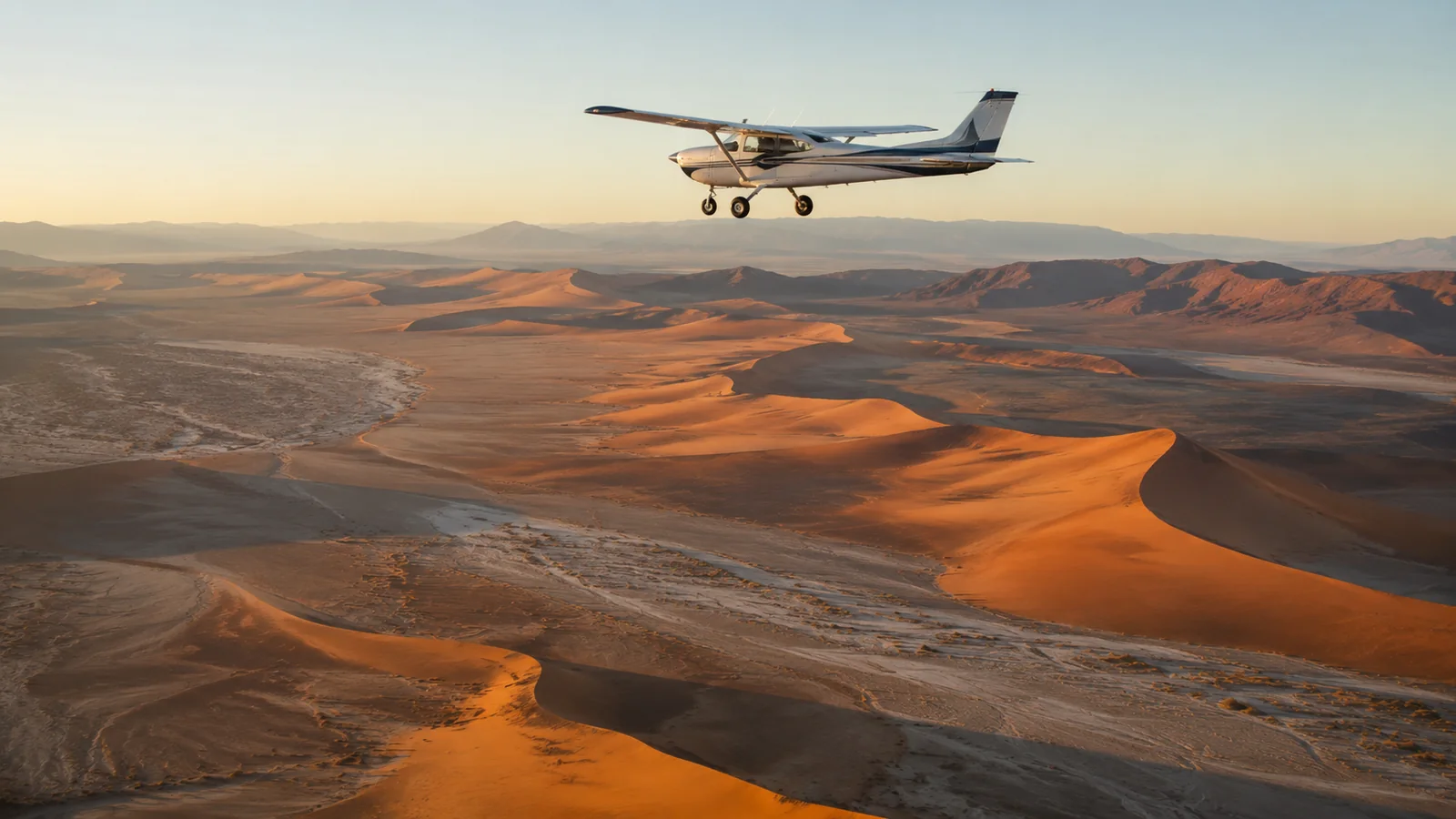 Small light aircraft flying low over the vast orange dunes and dry riverbeds of the Namib Desert Namibia at golden hour, aerial travel photography