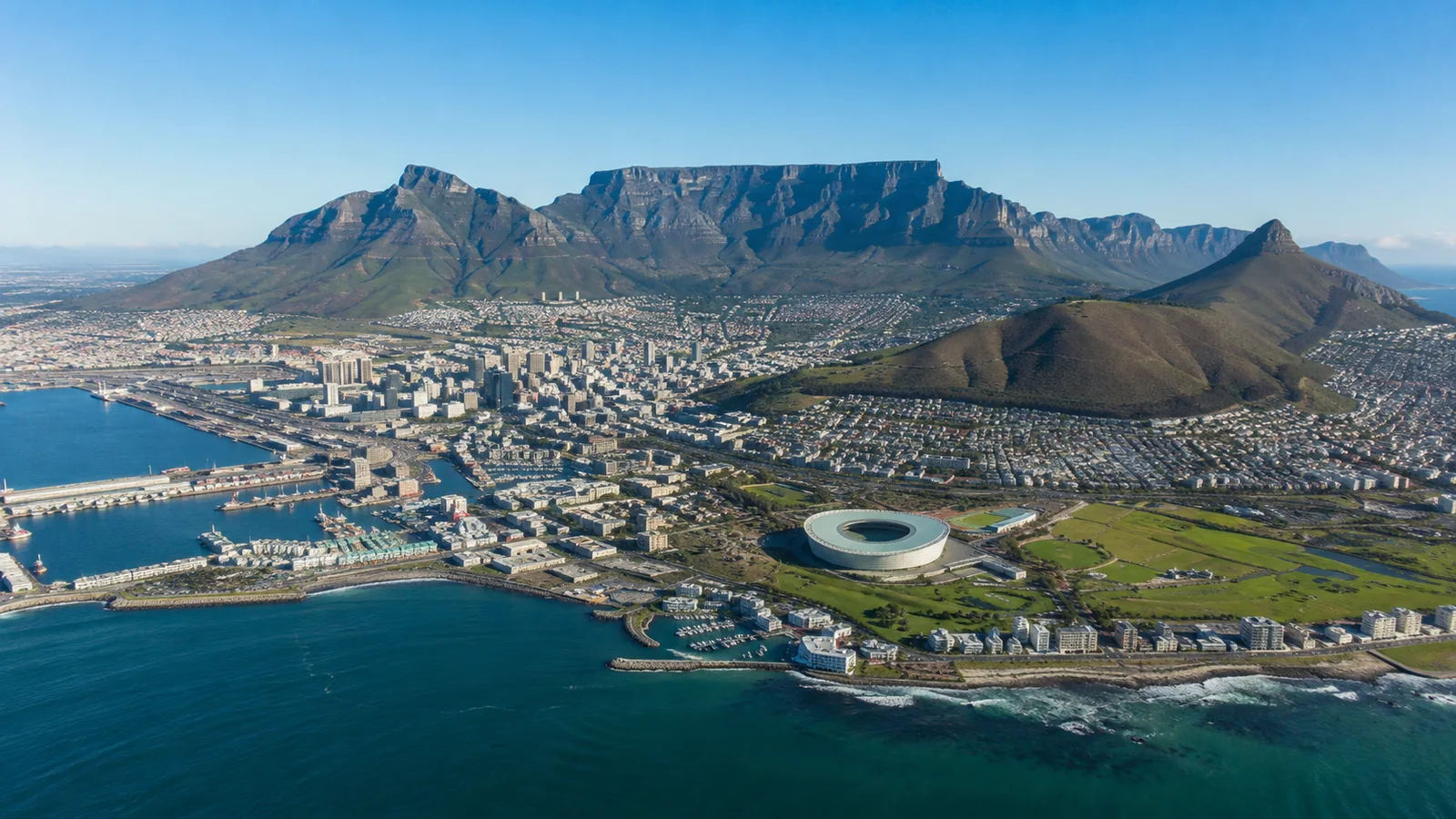 Aerial view of Cape Town with Table Mountain rising behind the city bowl and the Atlantic Ocean stretching to the horizon, bright clear-sky travel photography