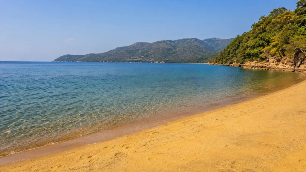 Malawi safari and lake — panoramic view of Lake Malawi's turquoise waters with golden sandy beach and lush green hills behind